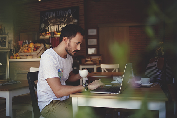Man working on his laptop remotely while drinking his coffee