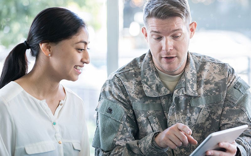 An army personnel interacting with a civilian using an apple device