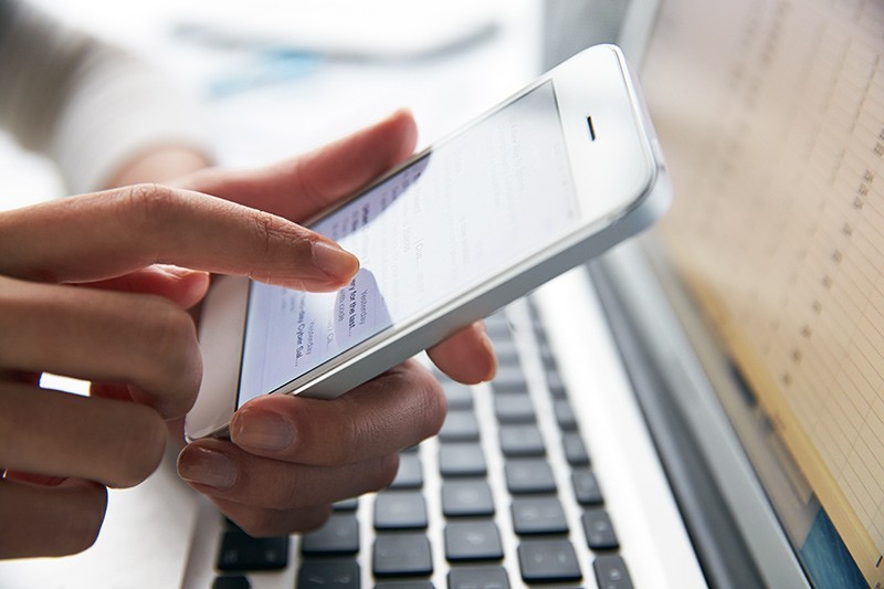Close up of a business professional using a smart phone while also on laptop computer