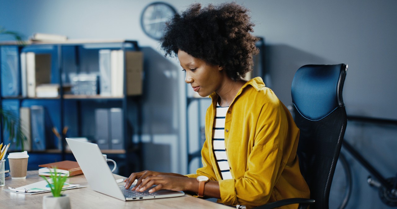 Beautiful joyful curly female worker typing on laptop and searching internet in cabinet. Pretty concentrated African American businesswoman working on computer while sitting at office. Job concept Beautiful joyful curly female worker typing on laptop and searching internet in cabinet. Pretty concentrated African American businesswoman working on computer while sitting at office. Job concept
