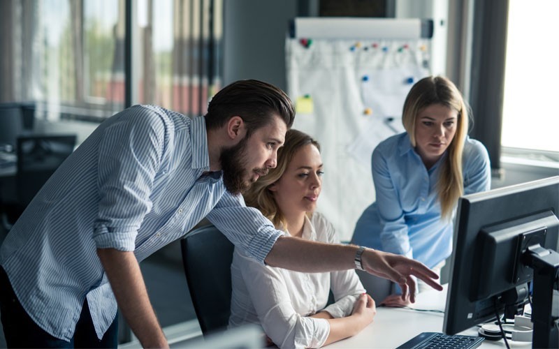 Ansible Automation takes these repetitive tasks and automates them Colleagues gather around desktop computer discussing automation tactics