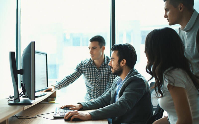 Red Hat takes a collaborative approach to technology Group of IT professionals gather around desktop computer in front of window