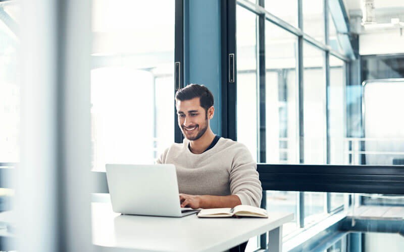Access the tools you need, when you need them, in any cloud environment Smiling man on laptop in modern open office