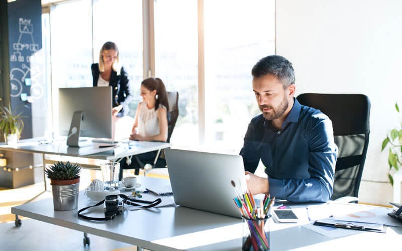 Deploy quickly while decreasing infrastructure costs Businessman on laptop device with coworkers working in background