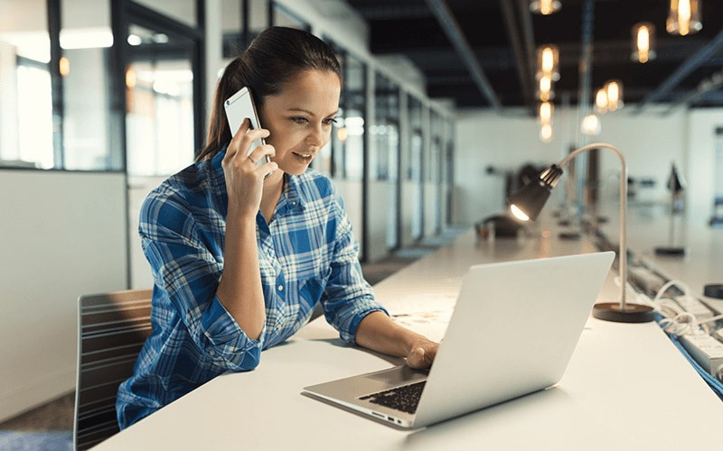 These tools help you develop apps fast and flexibly Smiling woman on mobile device with laptop computer at desk